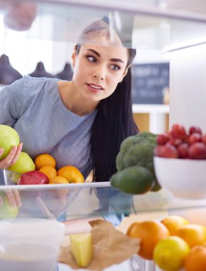 Gülümseyen kadın buzdolabından taze meyve alıyor, sağlıklı yiyecek konsepti.