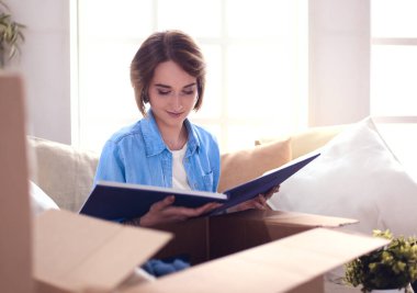 Genç bir kadın taşınıyor ve karton kutu paketliyor.