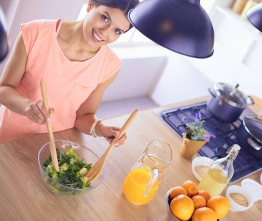 Gülümseyen genç kadın mutfakta taze salata karıştırıyor..
