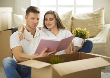 Yeni evlerinde karton kutuları açan sevimli bir çift yerde oturuyor ve bir aile albümüne bakıyor.