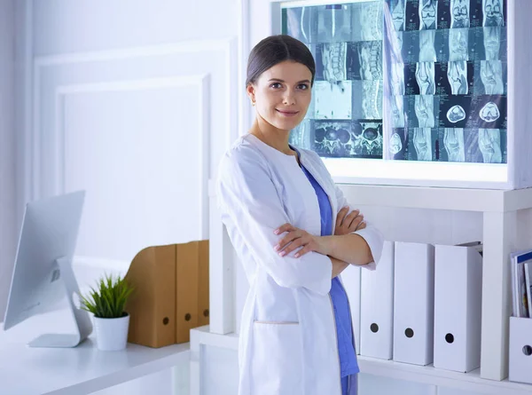 하얀 코트를 입고 손을 교차하여 병원에 서 있는 젊은 여성 의사의 모습 — 스톡 사진