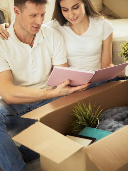 Leuk stel dat kartonnen dozen uitpakt in hun nieuwe huis, zittend op de vloer en kijkend naar een familiealbum — Stockfoto