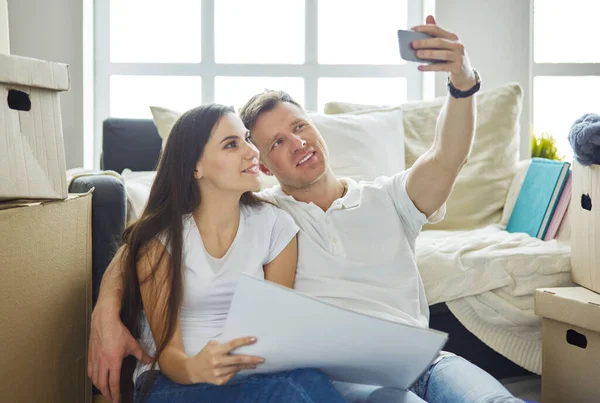 Unga par flyttar in i nytt hem tillsammans, sitter på golvet och gör selfies — Stockfoto