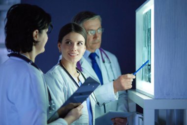 Bir grup doktor bir klinikte röntgenleri inceliyor, teşhis koymayı düşünüyorlar.