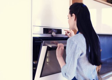 Güzel genç bayan pastasının fırında ne yaptığını kontrol ediyor.