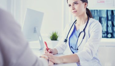 Kadın doktor hastane danışma odasında bir hastayı sakinleştiriyor, elini tutuyor.