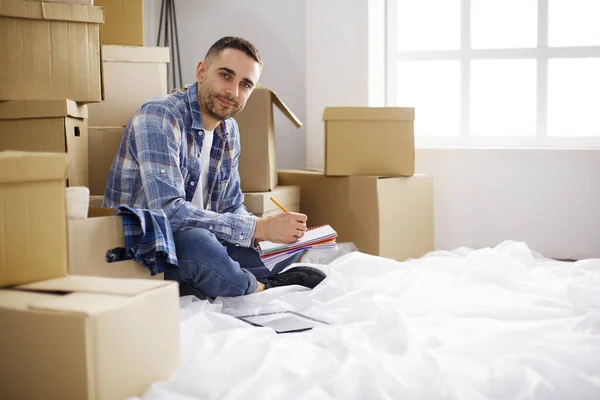 A moving man sitting on the floor in empty apartment, Among the Boxes, Checking the List of Things
