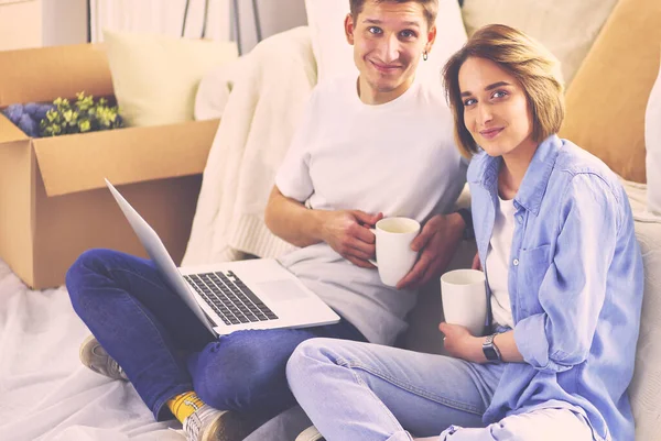 Casal compra on-line com um laptop e casa em movimento sentado no chão — Fotografia de Stock