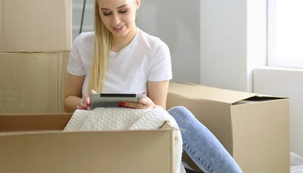 A beautiful single young woman unpacking boxes and moving into a new home. A women look at here tablet — Stock Photo, Image