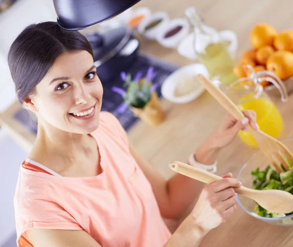 Улыбающаяся молодая женщина смешивает свежий салат на кухне. — стоковое фото