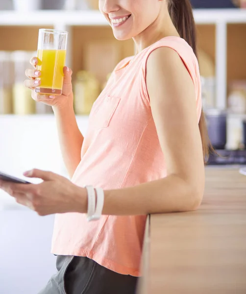 Cep telefonu görünümlü ve cam portakal suyu bir mutfakta Kahvaltı yaparken tutan gülümseyen güzel kadın. — Stok fotoğraf