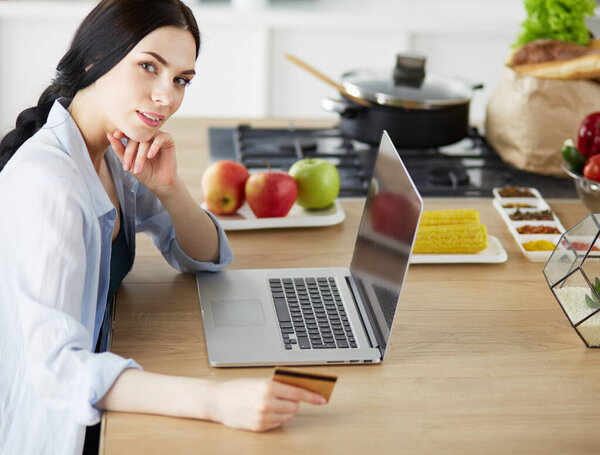 Smiling woman online shopping using computer and credit card in kitchen