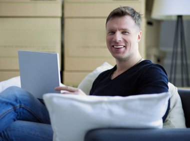 Yeni eve taşınan mutlu genç adamın portresi. Kollarında dijital tablet tutan bir adam.