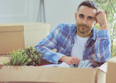 Taşınan bir adam boş bir dairede oturuyor, Kutuların arasında, eşyaların listesini kontrol ediyor.