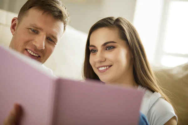 Nettes Paar beim Auspacken von Kartons in seinem neuen Zuhause, auf dem Boden sitzend und ein Familienalbum anschauend — Stockfoto