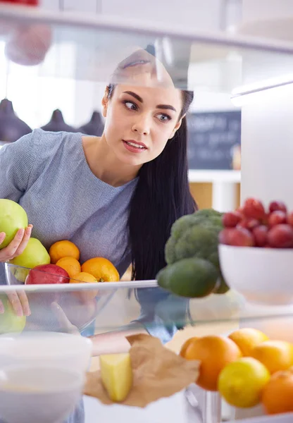 Smiling woman taking a fresh fruit out of the fridge, healthy food concept — Stock Photo, Image