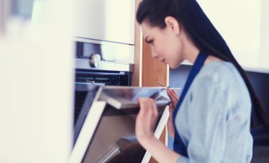 Güzel genç bayan pastasının fırında ne yaptığını kontrol ediyor.