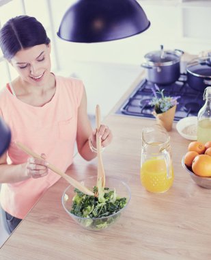 Gülümseyen genç kadın mutfakta taze salata karıştırıyor..