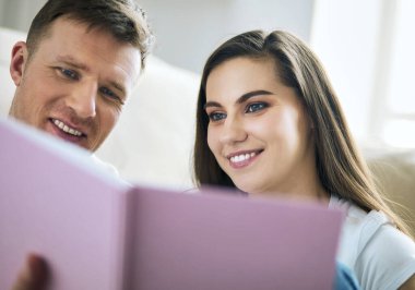 Yeni evlerinde karton kutuları açan sevimli bir çift yerde oturuyor ve bir aile albümüne bakıyor.