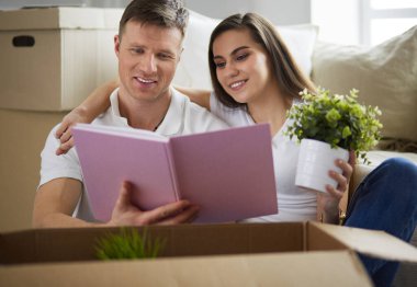 Yeni evlerinde karton kutuları açan sevimli bir çift yerde oturuyor ve bir aile albümüne bakıyor.