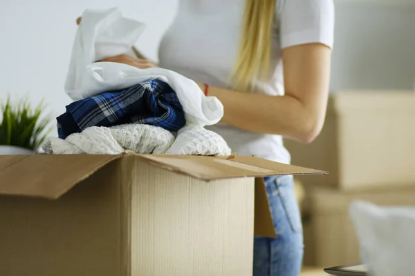 Een mooie alleenstaande jonge vrouw die dozen uitpakt en naar een nieuw huis verhuist. Een vrouw kijkt naar hier tablet — Stockfoto