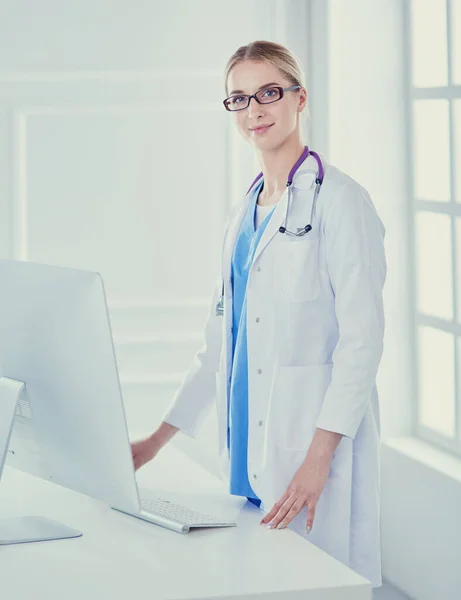 Mladý lékař žena stojící u stolu, izolované na bílém pozadí — Stock fotografie