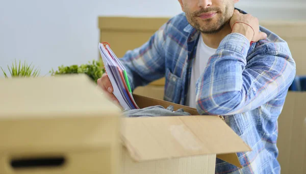 A moving man sitting on the floor in empty apartment, Among the Boxes, Checking the List of Things