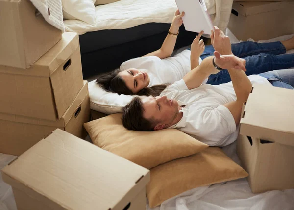 Linda pareja desempacando cajas de cartón en su nuevo hogar, tumbados en el suelo y mirando un álbum familiar —  Fotos de Stock