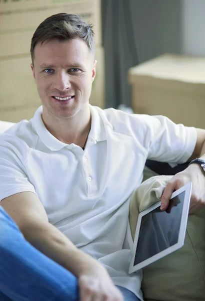 Retrato de un joven feliz mudándose a un nuevo hogar. Hombre sosteniendo tableta digital en sus brazos —  Fotos de Stock