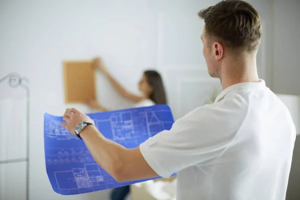 Vrouw helpt haar partner om schilderij te hangen aan de muur van hun nieuwe huis, ze is framing de foto met haar vingers — Stockfoto