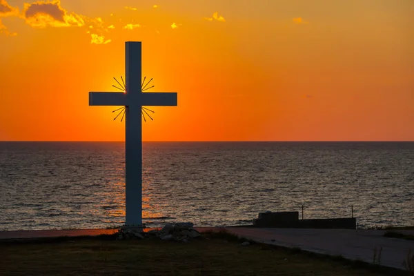 Silueta de cruz al amanecer o al atardecer con rayos de luz y vistas al mar — Foto de Stock