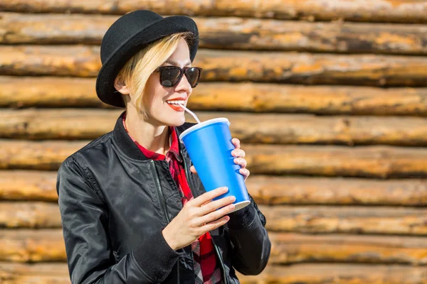 Glimlachend modieuze blonde drinken cola buitenshuis op houten achtergrond — Stockfoto