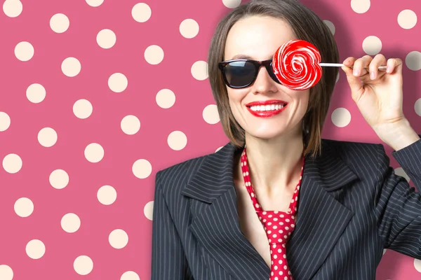 Красивая женщина в солнечных очках есть конфеты lolippop над ярко-красной горошек фон — стоковое фото