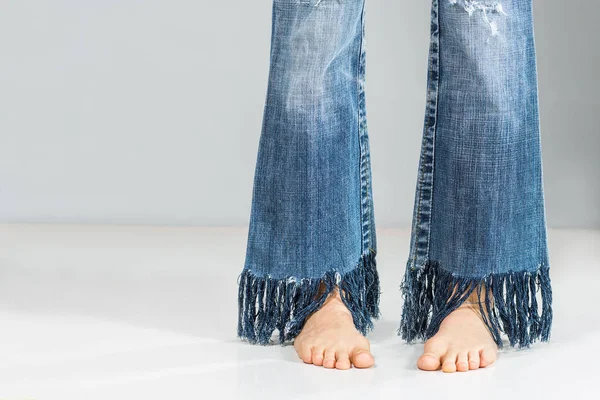 灰色の背景の上のフリンジ付きジーンズを着て裸足のセクシーな美脚 — ストック写真