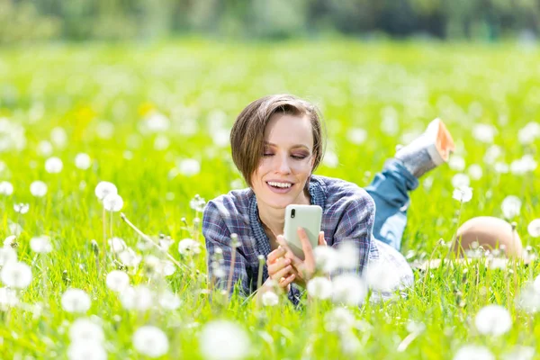 Ung kvinna med hjälp av mobiltelefon i en våren äng — Stockfoto