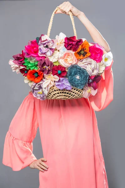 Mooie vrouw in roze jurk die bloemen tas geïsoleerd over grijs — Stockfoto