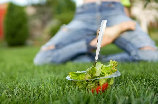 Зелений салат на зеленій траві з дівчиною йоги на фоні — стокове фото