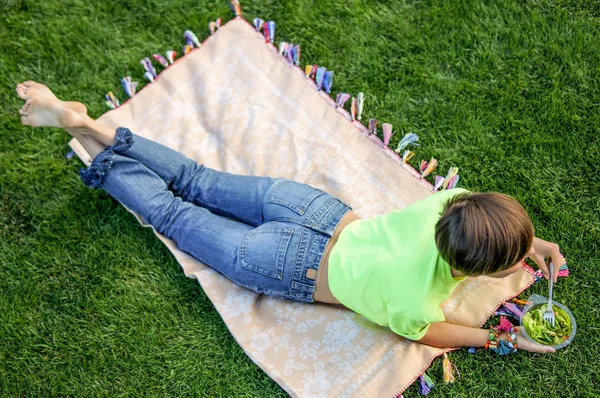 Jovem mulher comendo salada relaxante ao ar livre sentado na grama verde — Fotografia de Stock