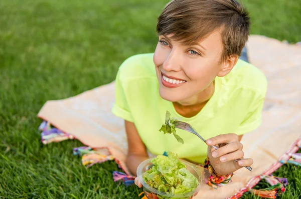 Giovane donna mangiare insalata rilassante all'aperto seduti su erba verde — Foto Stock