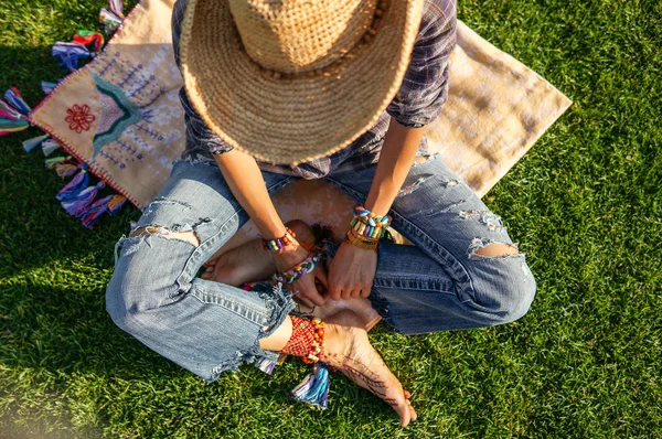 Bovenaanzicht van jonge vrouw die het dragen van jeans en hoed zittend op groen gras — Stockfoto