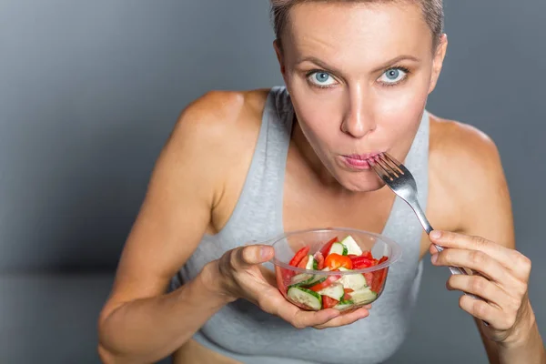 Funny woman eating salad over grey background,