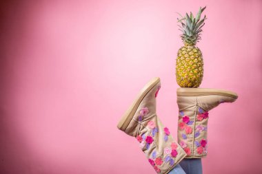 Botları ve ananas pembe arka plan üzerinde tutarak sevimli kadın ayakları