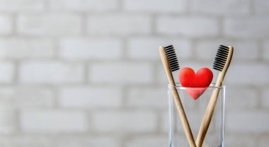 Camda iki diş fırçası ve tuğla duvar arkasında kırmızı kalp. Aşk ve Sevgililer Günü konsepti. Bambu çevre dostu diş fırçaları.