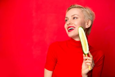 Mutlu genç kadın salatalık kırmızı duvar arka plan üzerinde yemek