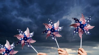 Patriotic people holding pinwheels with amercian flag over dramatic cloudy sky. Independence day, veterans day, copy space clipart