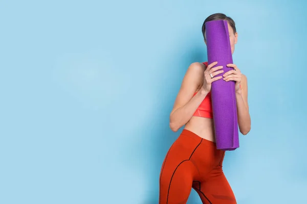 Funny playful fitness girl hiding face with yoga mat