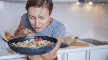 Young woman going to eat rice with vegetables, smelling delicious aroma from just prepared food