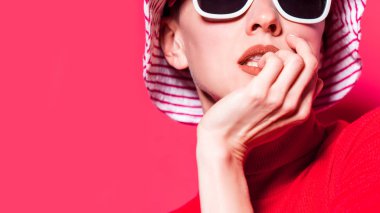 Parlak moda konsepti. Çizgili şapkalı, pembe arka planda güneş gözlüklü güzel bir kız.