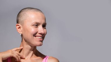 Gri arka plan duvarında kendine güvenen güzel, mutlu, kel bir kadın.