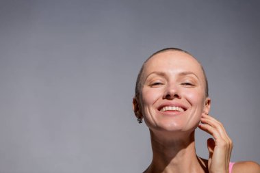 Gri arka plan duvarında kendine güvenen güzel, mutlu, kel bir kadın.